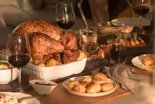 Thanksgiving table with turkey, biscuits, wine and side dishes